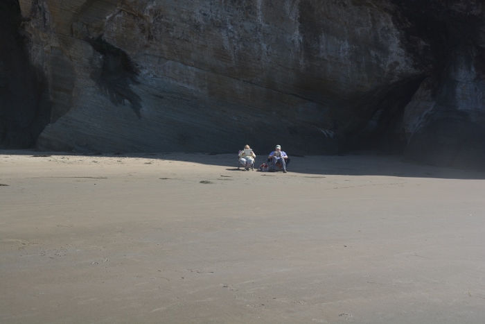 Couple sitting in chairs reading in front of massive rock wall on beach